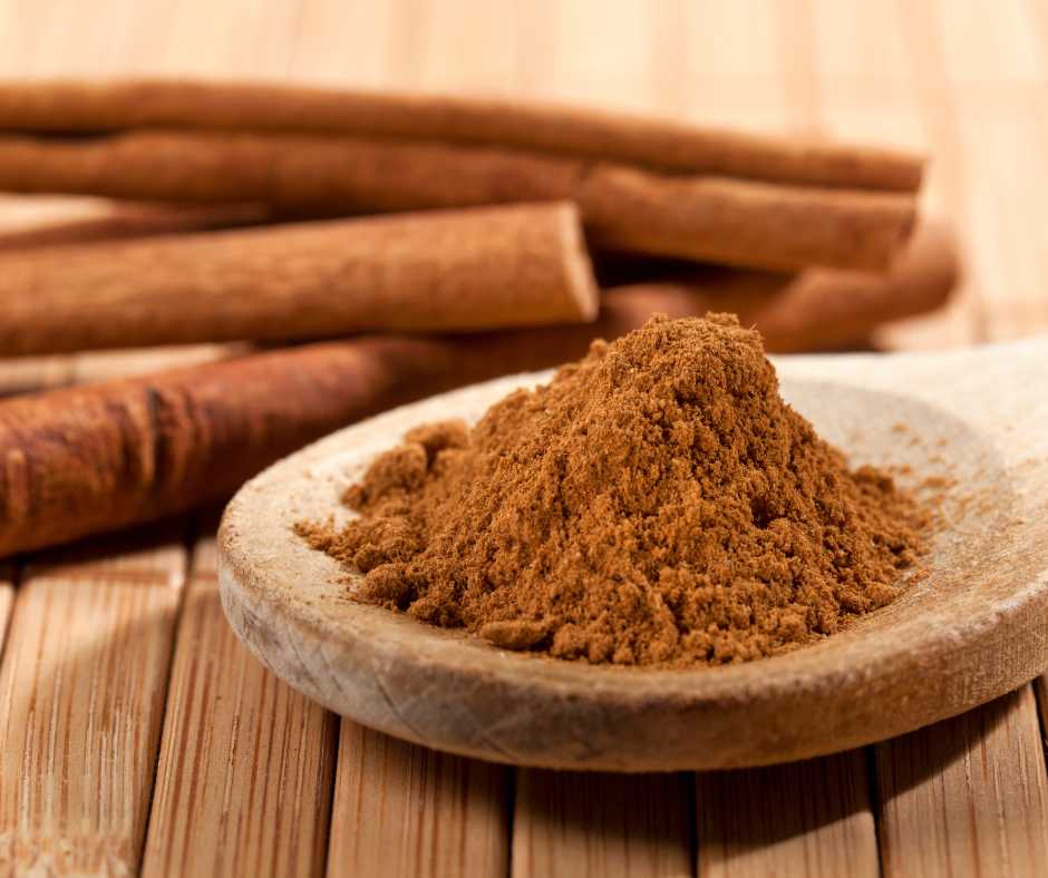A close-up view of ground cinnamon on a wooden spoon and cinnamon sticks, showcasing the spice's texture and warm color.