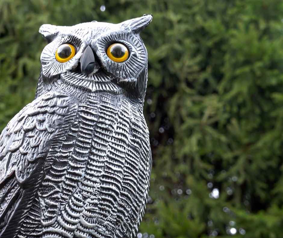 A realistic fake owl decoy perched in a garden, designed to deter pests and protect the environment.