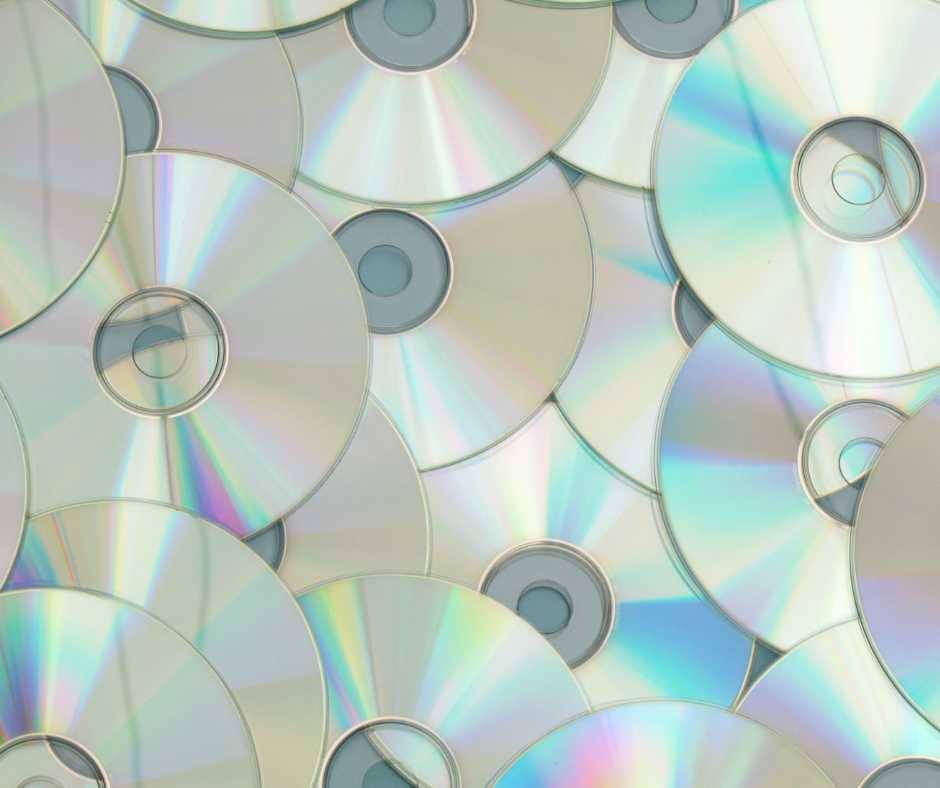 A multitude of compact discs (CDs) scattered, showcasing their reflective surfaces that create a rainbow spectrum of colors, often associated with data storage and music playback.