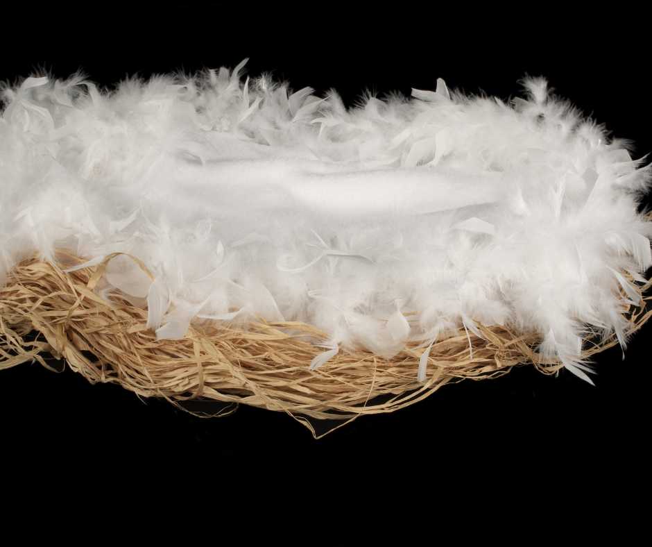 A handmade bird nest adorned with soft white feathers and tissue on a contrasting black background.